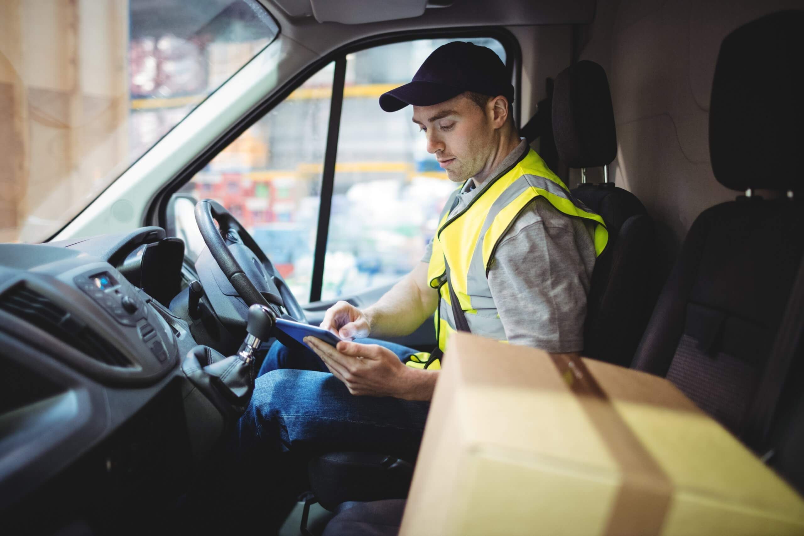 Delivery driver using tablet in van with parcels on seat