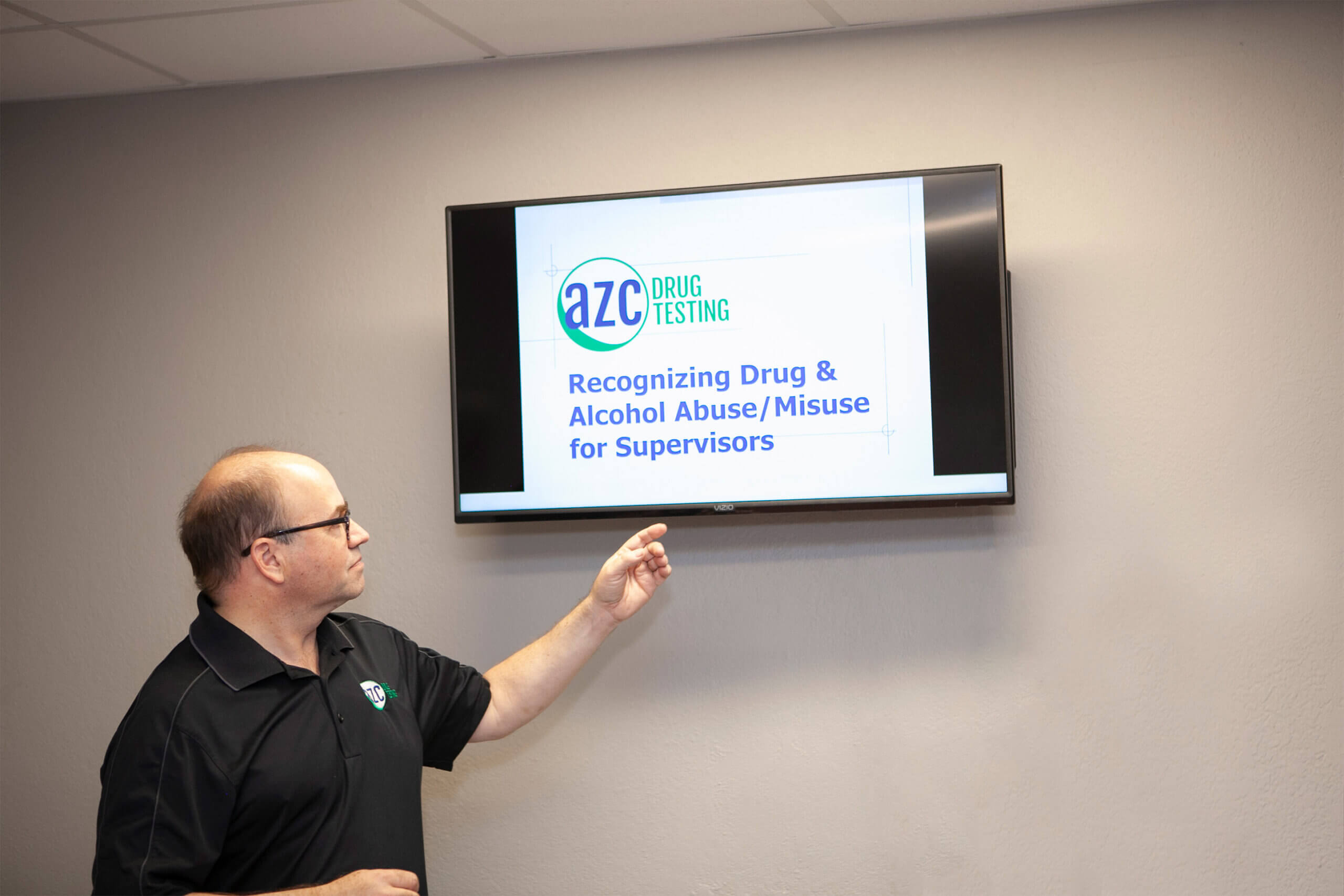 A man pointing to a tv screen with a presentation about recognizing drug and alcohol abuse