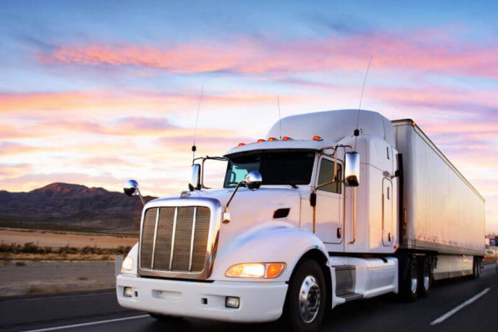 A semi-truck travelling through the desert at sunset