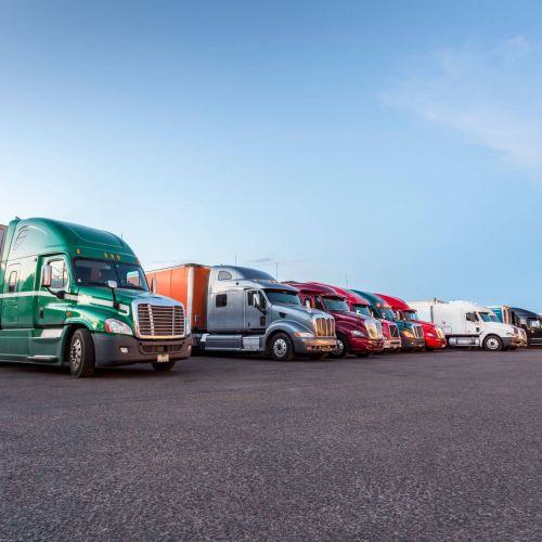 A row of different colored semi-trucks parked at a truck stop