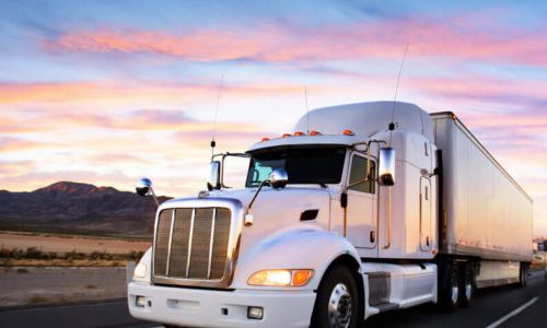 A semi-truck travelling through the desert at sunset